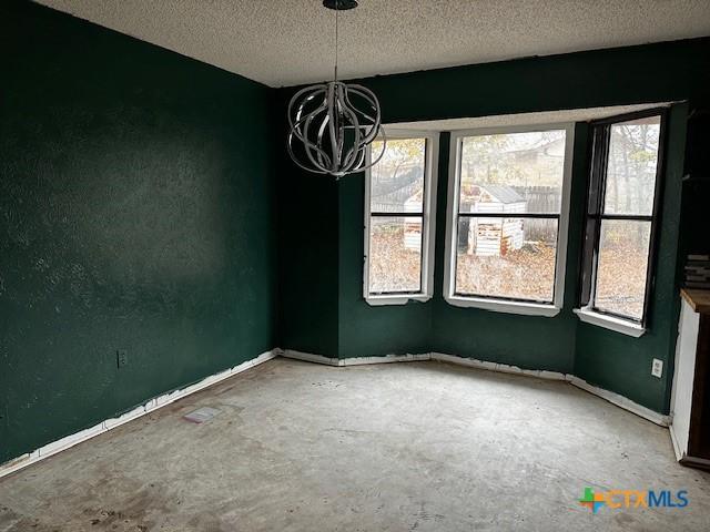 unfurnished room featuring concrete flooring, a textured ceiling, a wealth of natural light, and a chandelier