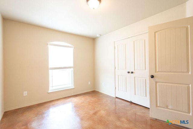 unfurnished bedroom featuring finished concrete floors, a closet, and baseboards