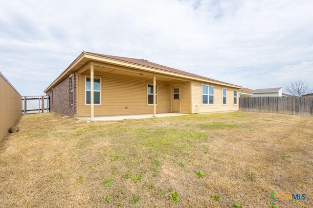 rear view of property featuring brick siding, a yard, fence, and a patio