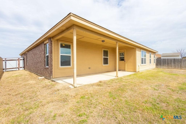 rear view of property featuring brick siding, a lawn, a gate, a patio area, and a fenced backyard