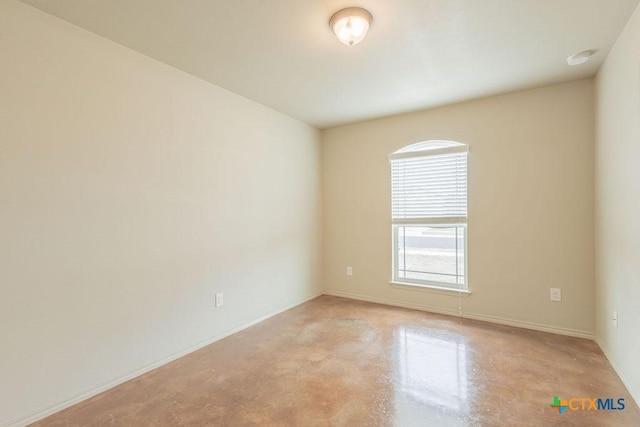 spare room featuring finished concrete flooring and baseboards