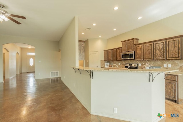 kitchen with arched walkways, appliances with stainless steel finishes, a kitchen bar, and decorative backsplash