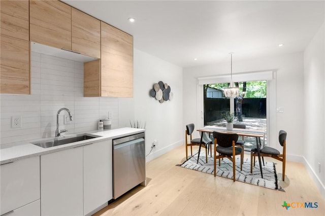 kitchen featuring dishwasher, a sink, backsplash, baseboards, and light wood finished floors