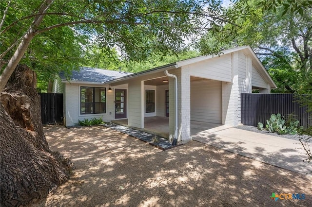 view of front facade with brick siding, driveway, fence, a patio, and roof with shingles
