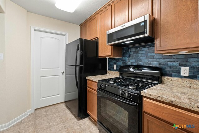 kitchen featuring light tile patterned floors, black appliances, light stone counters, and tasteful backsplash