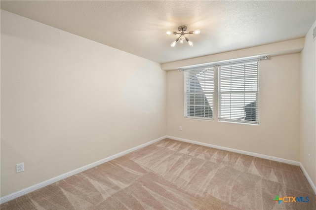 empty room featuring a textured ceiling, carpet flooring, and a notable chandelier