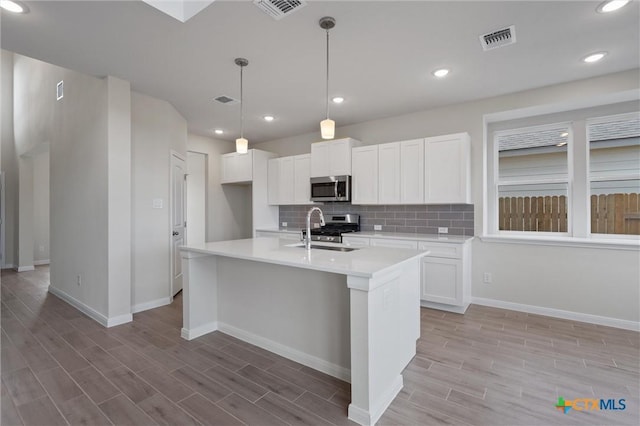 kitchen with stainless steel appliances, sink, decorative light fixtures, a center island with sink, and white cabinetry