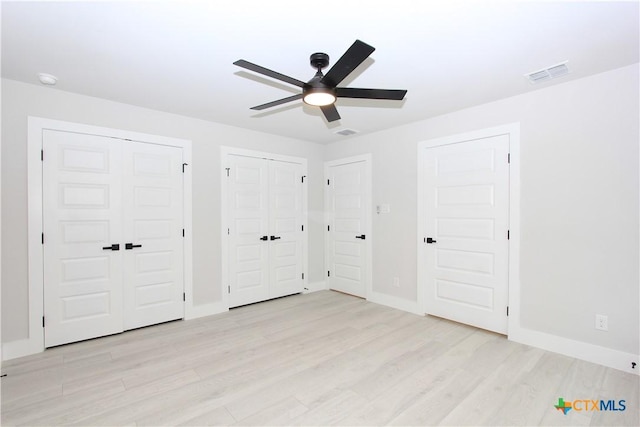 unfurnished bedroom with light wood-type flooring, baseboards, visible vents, and multiple closets