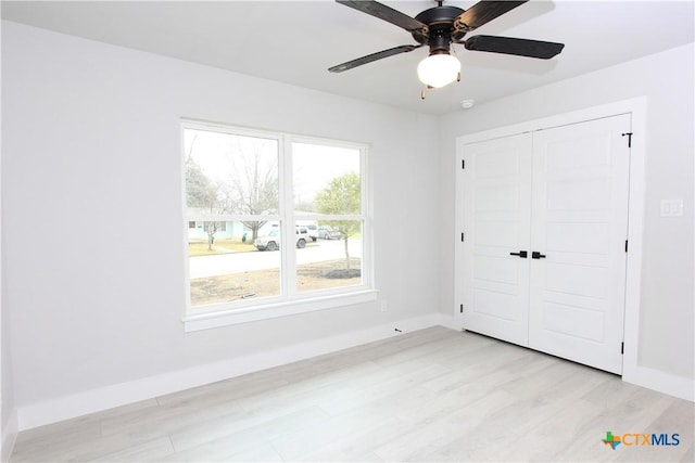 unfurnished bedroom with light wood-style floors, a closet, baseboards, and a ceiling fan