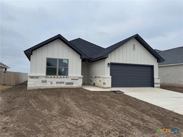 modern farmhouse with a garage, a shingled roof, concrete driveway, stone siding, and board and batten siding