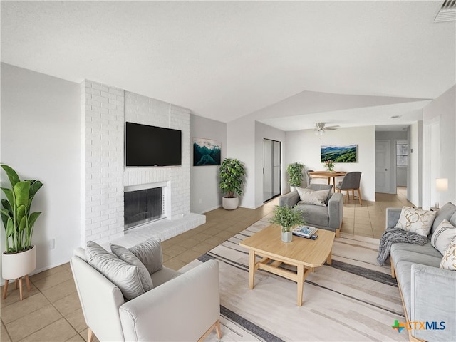 living room with ceiling fan, light tile patterned flooring, vaulted ceiling, and a brick fireplace