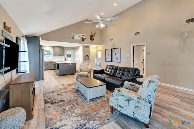 living room with ceiling fan, light hardwood / wood-style floors, and high vaulted ceiling