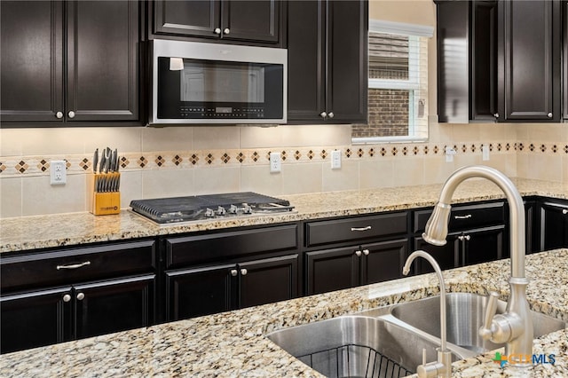 kitchen with tasteful backsplash, light stone countertops, appliances with stainless steel finishes, dark cabinetry, and a sink