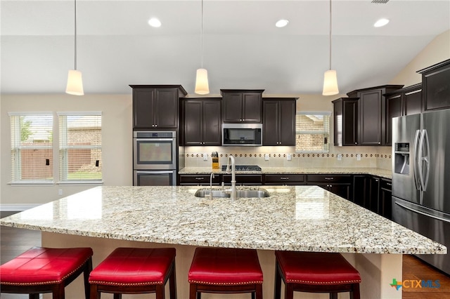 kitchen with light stone countertops, a sink, stainless steel appliances, and decorative backsplash