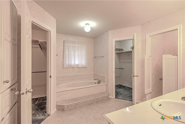 bathroom with tile patterned floors, vanity, a bath, and a textured ceiling