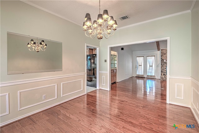 unfurnished dining area featuring ornamental molding, a textured ceiling, hardwood / wood-style flooring, and a notable chandelier