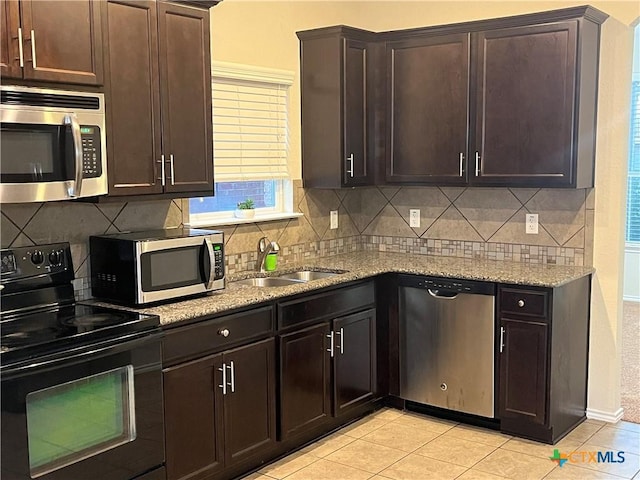 kitchen with appliances with stainless steel finishes, tasteful backsplash, sink, light stone counters, and dark brown cabinets