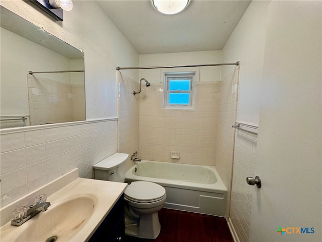 full bathroom with tiled shower / bath, wood-type flooring, vanity, toilet, and tile walls