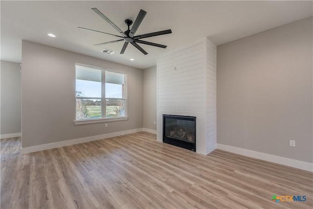 unfurnished living room with a large fireplace, ceiling fan, and light hardwood / wood-style flooring