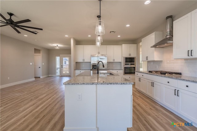 kitchen with wall chimney exhaust hood, an island with sink, hanging light fixtures, and white cabinets