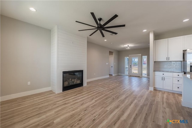 unfurnished living room with ceiling fan, a large fireplace, and light hardwood / wood-style floors