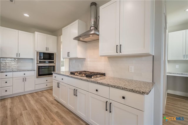 kitchen with wall chimney range hood, appliances with stainless steel finishes, white cabinets, decorative backsplash, and light wood-type flooring