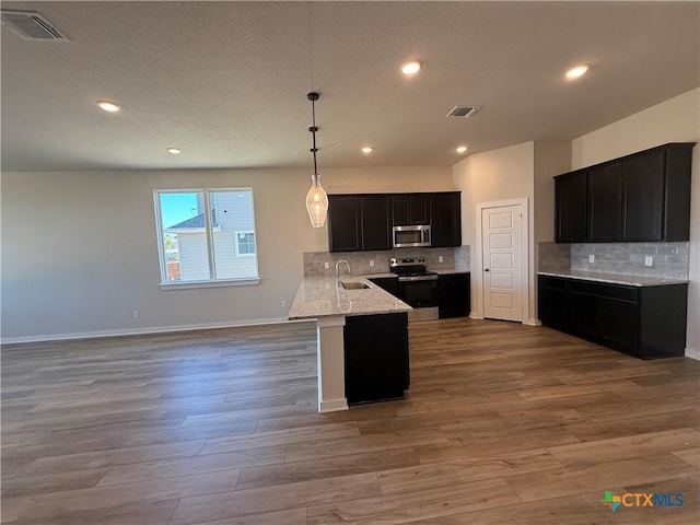 kitchen featuring stainless steel appliances, wood-type flooring, hanging light fixtures, and kitchen peninsula