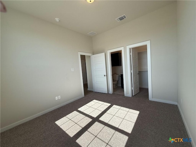 unfurnished bedroom featuring ensuite bath, a spacious closet, dark carpet, and a closet