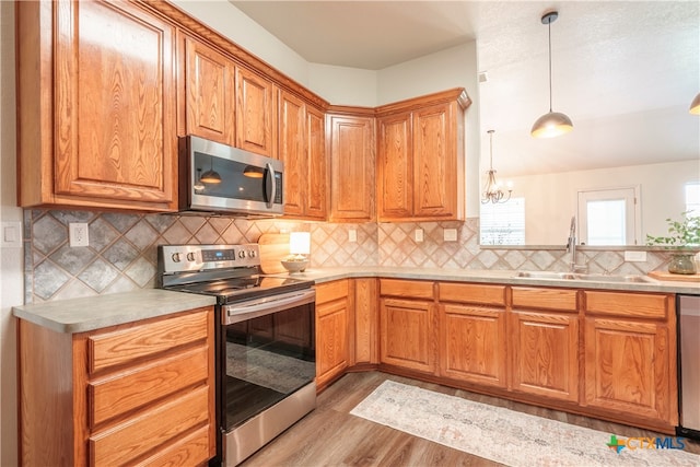 kitchen with stainless steel appliances, light hardwood / wood-style floors, sink, tasteful backsplash, and pendant lighting