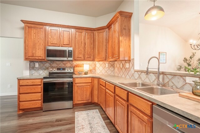 kitchen with stainless steel appliances, hardwood / wood-style flooring, sink, tasteful backsplash, and hanging light fixtures