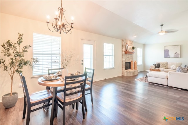 dining room featuring dark hardwood / wood-style flooring, a stone fireplace, lofted ceiling, and ceiling fan with notable chandelier