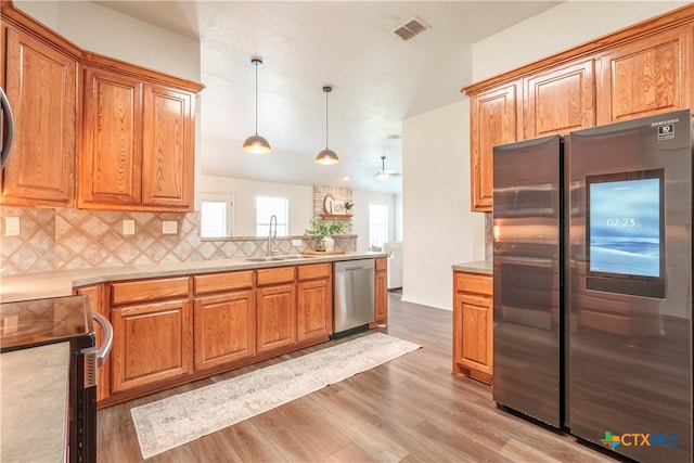 kitchen featuring tasteful backsplash, appliances with stainless steel finishes, pendant lighting, sink, and light hardwood / wood-style flooring