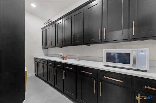 kitchen featuring recessed lighting, light countertops, white microwave, dark cabinetry, and baseboards