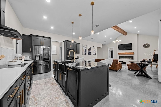 kitchen with an island with sink, dark cabinetry, wall chimney range hood, and black appliances