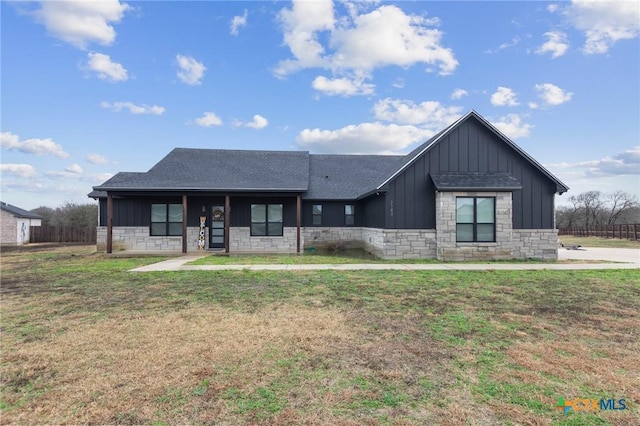 view of front of house with board and batten siding, stone siding, roof with shingles, and a front lawn