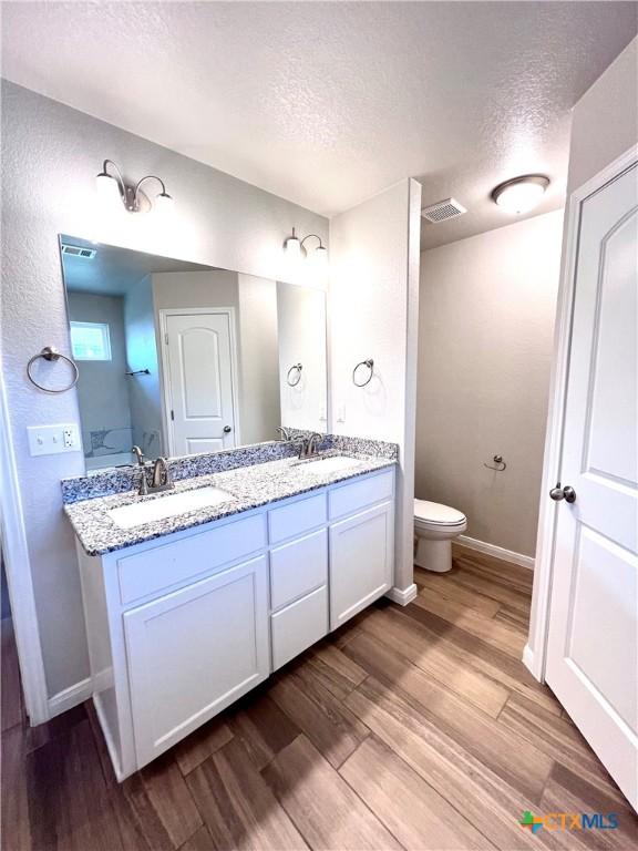 8302 Ridge Crest Dr, Killeen, TX 76542 - full bathroom featuring a textured ceiling, double vanity, wood finished floors, toilet, and baseboards