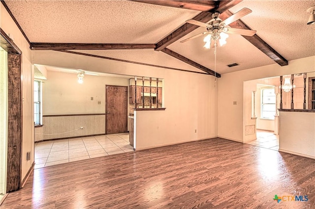 empty room with a ceiling fan, a wainscoted wall, wood finished floors, and a textured ceiling