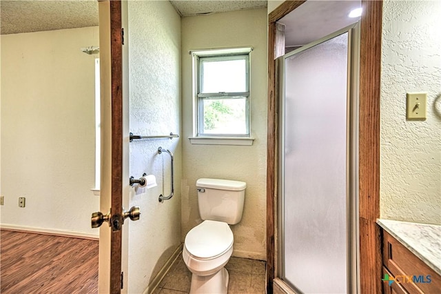 full bathroom featuring toilet, wood finished floors, a shower stall, a textured wall, and vanity