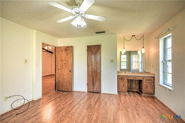 unfurnished bedroom with wood finished floors, a textured ceiling, multiple windows, and visible vents
