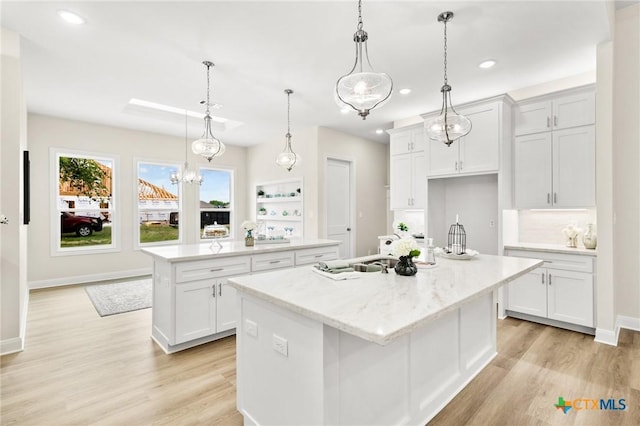kitchen with recessed lighting, decorative light fixtures, light wood-style floors, white cabinetry, and a center island with sink