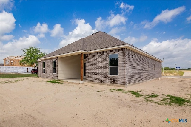 rear view of house with roof with shingles and brick siding