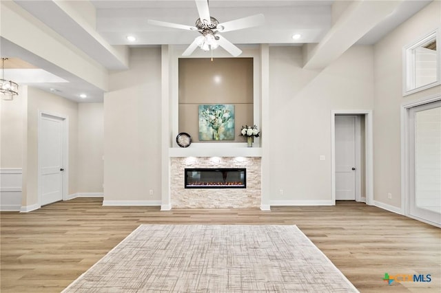 unfurnished living room featuring ceiling fan with notable chandelier, baseboards, a glass covered fireplace, and wood finished floors