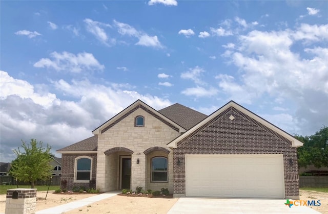 view of front of property with an attached garage, stone siding, fence, brick siding, and driveway