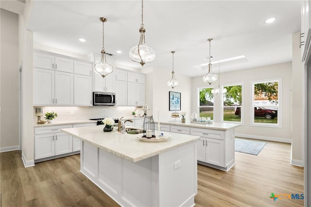 kitchen with stainless steel microwave, a sink, an island with sink, white cabinetry, and backsplash