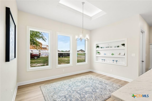 dining space with baseboards, light wood-style flooring, a chandelier, and a skylight