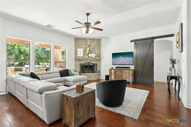 living area featuring a barn door, dark wood finished floors, visible vents, and ceiling fan