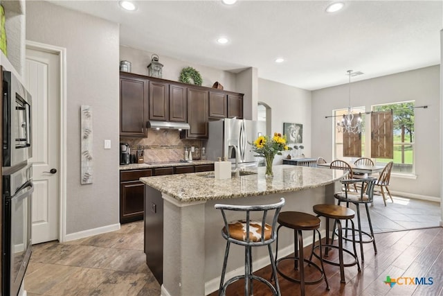 kitchen featuring a sink, a center island with sink, dark brown cabinetry, a kitchen bar, and appliances with stainless steel finishes