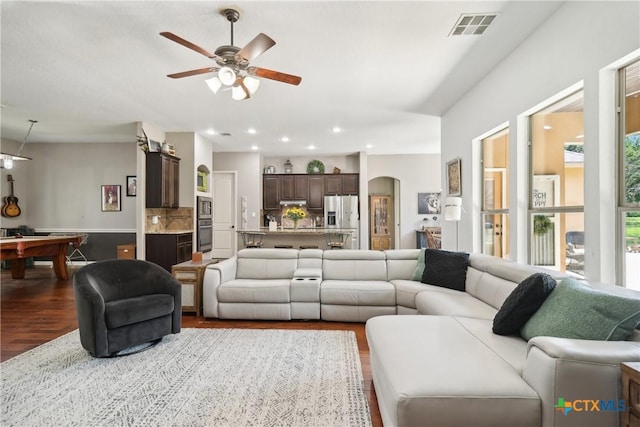 living room featuring plenty of natural light, a ceiling fan, visible vents, and dark wood finished floors