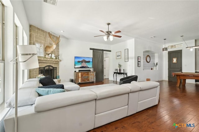 living area with a barn door, wood finished floors, visible vents, a ceiling fan, and a fireplace