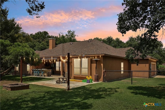 rear view of property with fence, an outdoor kitchen, a lawn, a patio, and stucco siding